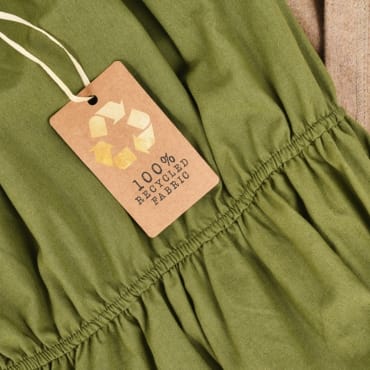 A close-up of a green fabric garment with a tag indicating "100% recycled fabric," showing gathered stitching detail.