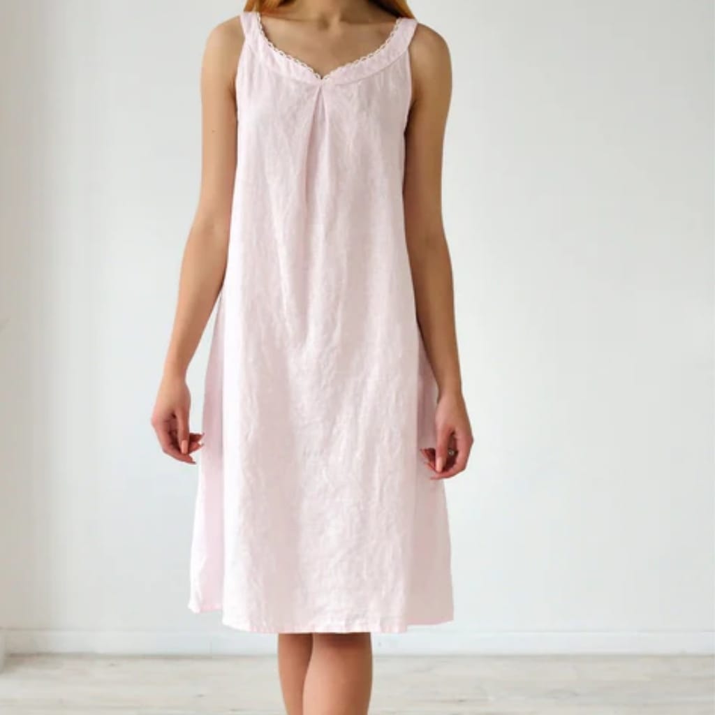 A person is wearing a light pink sleeveless dress with a scalloped V-neckline, standing against a plain white background.