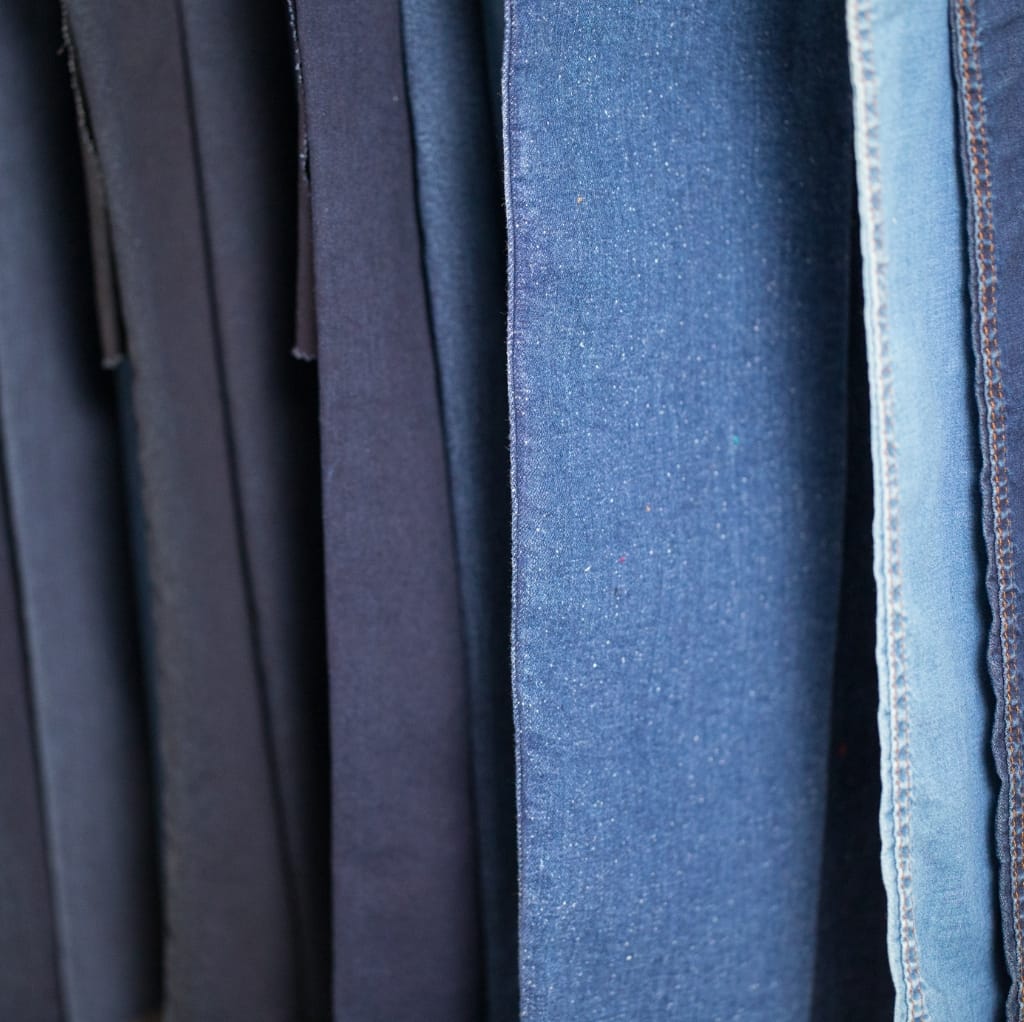 Close-up of several denim fabrics hanging on a rack, showcasing various shades of blue and different textures.