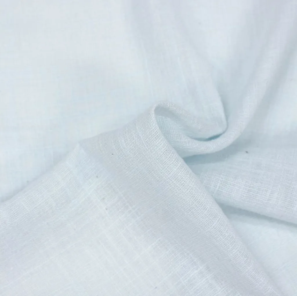 Close-up image of light-colored, semi-sheer cotton voile fabric with a soft, smooth, and slightly textured surface, gently folded to show its lightweight and airy quality.