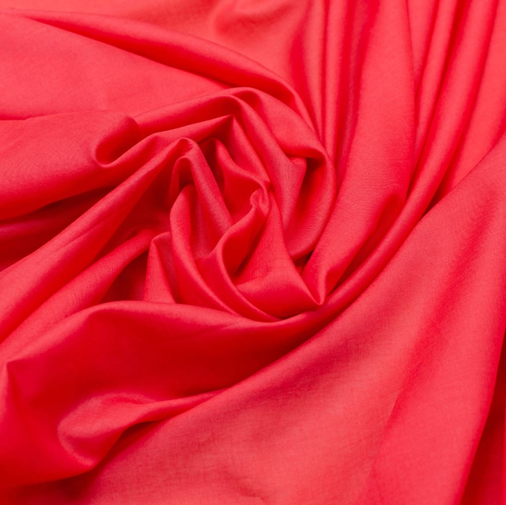 Close-up image of soft, bright coral-colored cotton batiste fabric with gentle folds and drapes.