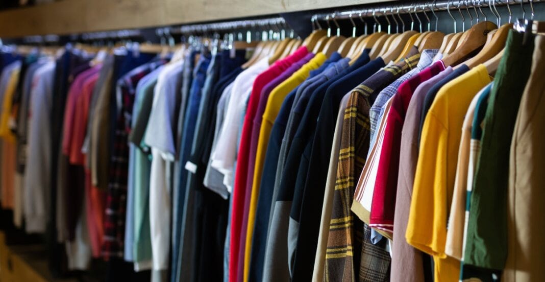 A row of colorful men's and women's casual T-shirts and shirts hanging on wooden hangers in a wholesale clothing store. Garment Cotton Fabric Wholesale