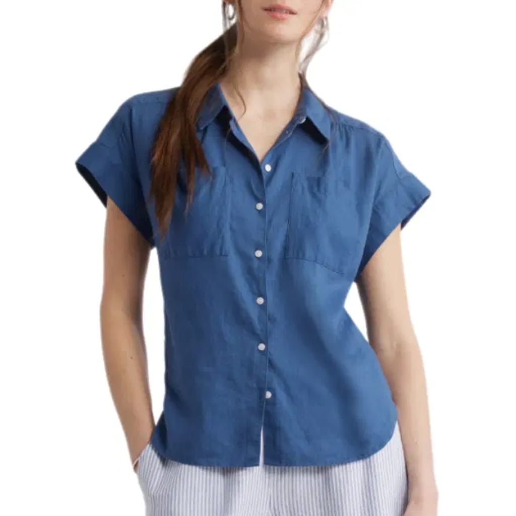 A woman is wearing a short-sleeved, button-up denim shirt with a collar. The background is white, and her face is partially visible.