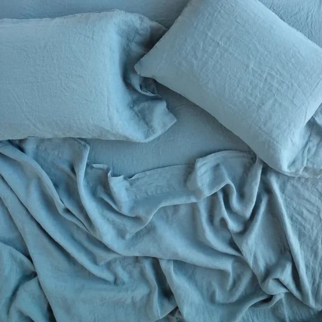 A crumpled, light blue bedsheet with two matching pillows, creating a textured, slightly messy appearance.