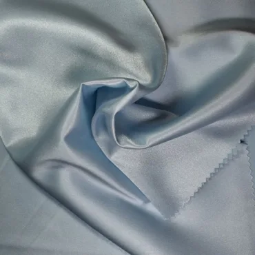Close-up of light blue, shiny 100% polyester fabric with a smooth, silky texture, gently folded to showcase its sheen and drape.