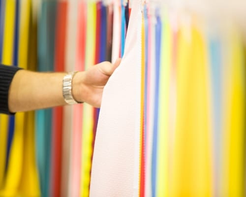 A person holding a piece of white fabric in front of a colorful display of fabric rolls in a store or warehouse.