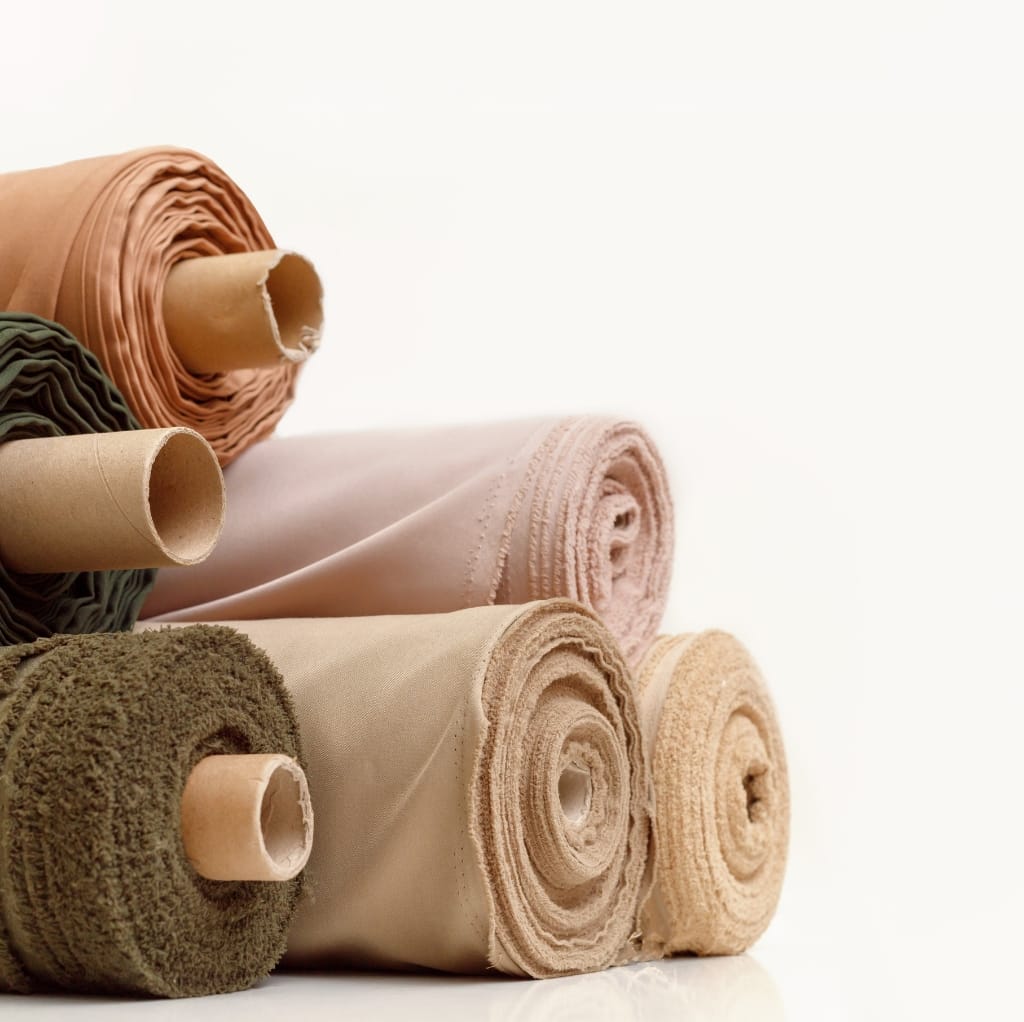 A close-up image of several cotton fabric rolls in various colors, stacked horizontally on a white surface.