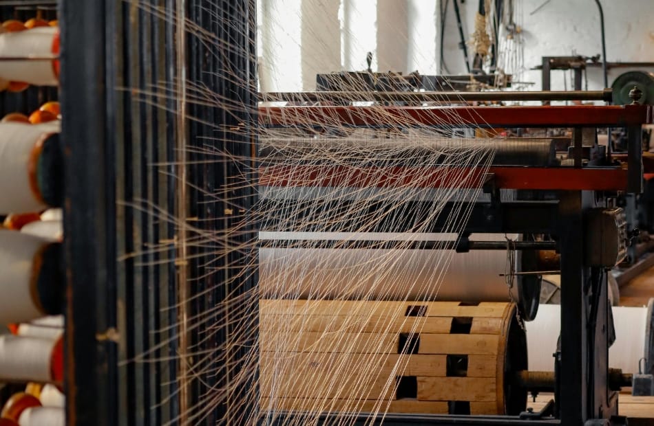 Close-up of textile manufacturing machinery weaving multiple threads, showcasing modern technology in American textile production. American Made Textiles