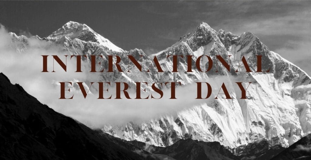 Black and white photograph of the towering, snow-covered Himalayan mountains, with the text "International Everest Day" overlaid in large, bold brown letters.