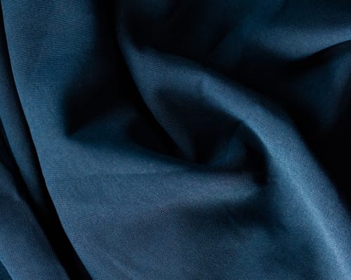 A close-up image of smooth, dark blue, static-free cotton fabric with gentle folds.