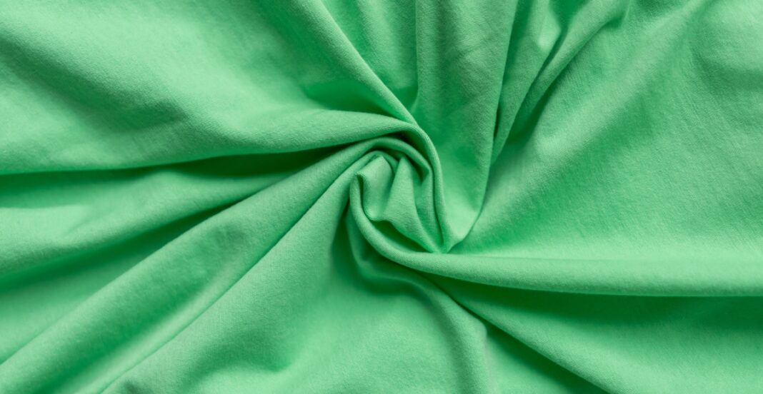 A close-up image of a soft, green jersey cotton fabric with gentle folds and a smooth texture.