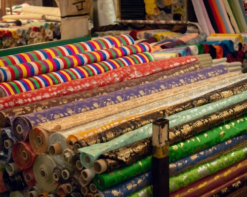 A colorful display of various rolls of patterned and plain cotton fabric stacked on a table in a fabric store.
