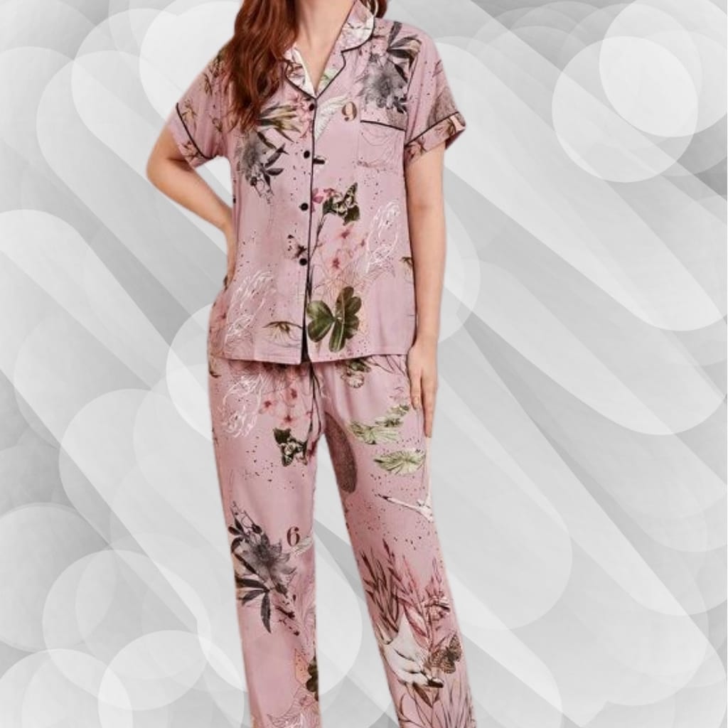 A woman wearing pink floral pajamas with a short-sleeved, button-up top and matching wide-leg pants, standing against a light-colored, abstract background.