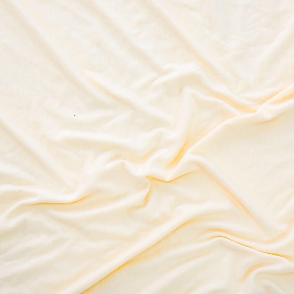 A close-up of soft, cream-colored satin fabric with gentle folds and a smooth, shiny texture.