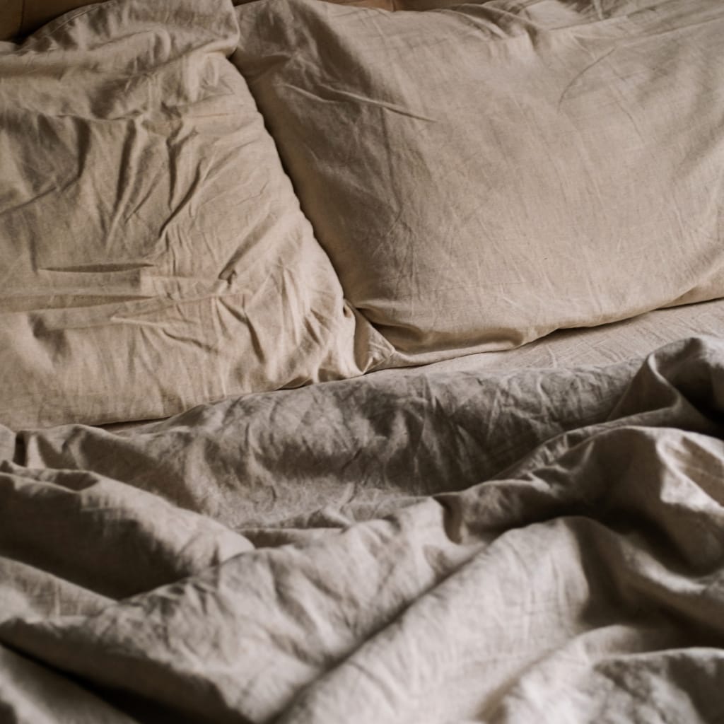 An unmade bed with beige, wrinkled sheets and pillowcases. The bedding appears slightly disheveled and rumpled.
