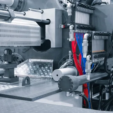 Close-up of an industrial machine in a PET recycling or manufacturing facility, featuring pipelines, heating elements, and extruder components.
