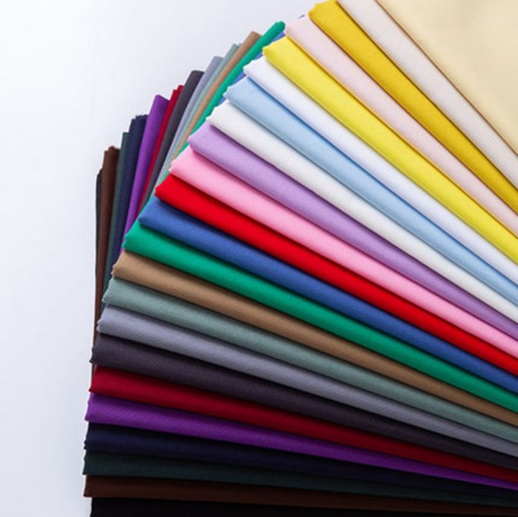 A colorful fan of folded plain weave cotton fabric samples arranged in a semi-circle on a white surface.