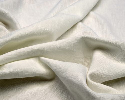 Cream-colored, soft, textured organic cotton fabric with gentle folds and a natural weave. Leading Cotton Fabric Manufacturers