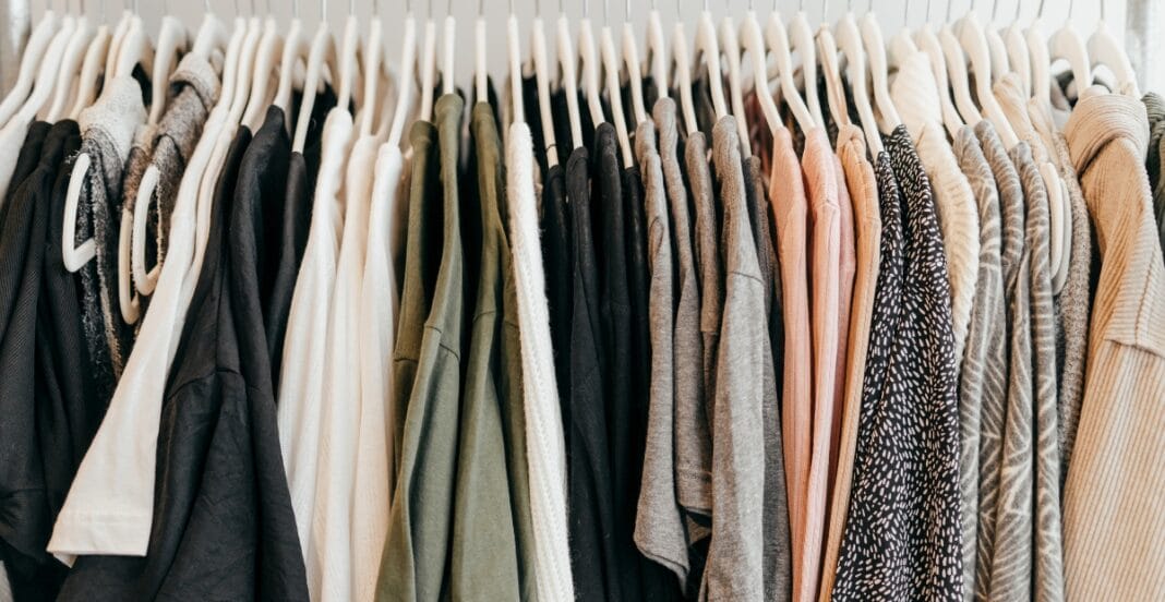 A row of various polyester clothes hanging on white hangers, including T-shirts, blouses, and jackets in different colors and patterns.