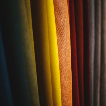 A close-up of vertically hanging fabric swatches in various colors including dark green, yellow, orange, red, and brown.