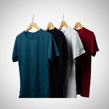 A display of four plain T-shirts in different colors (blue, black, white, and red) hanging on wooden hangers against a neutral background.