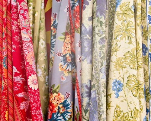 Close-up of various printed cotton fabrics hanging side by side, showcasing an array of floral and decorative patterns in multiple colors like red, blue, green, and yellow.