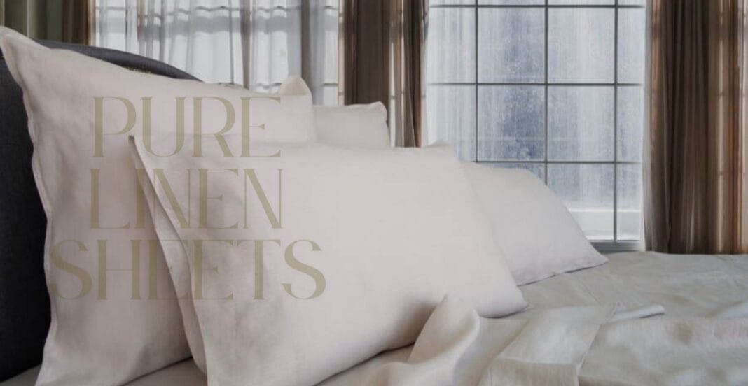 A cozy bed with neatly arranged white linen sheets and matching pillowcases, set in front of large windows with sheer curtains, allowing natural light to fill the room.