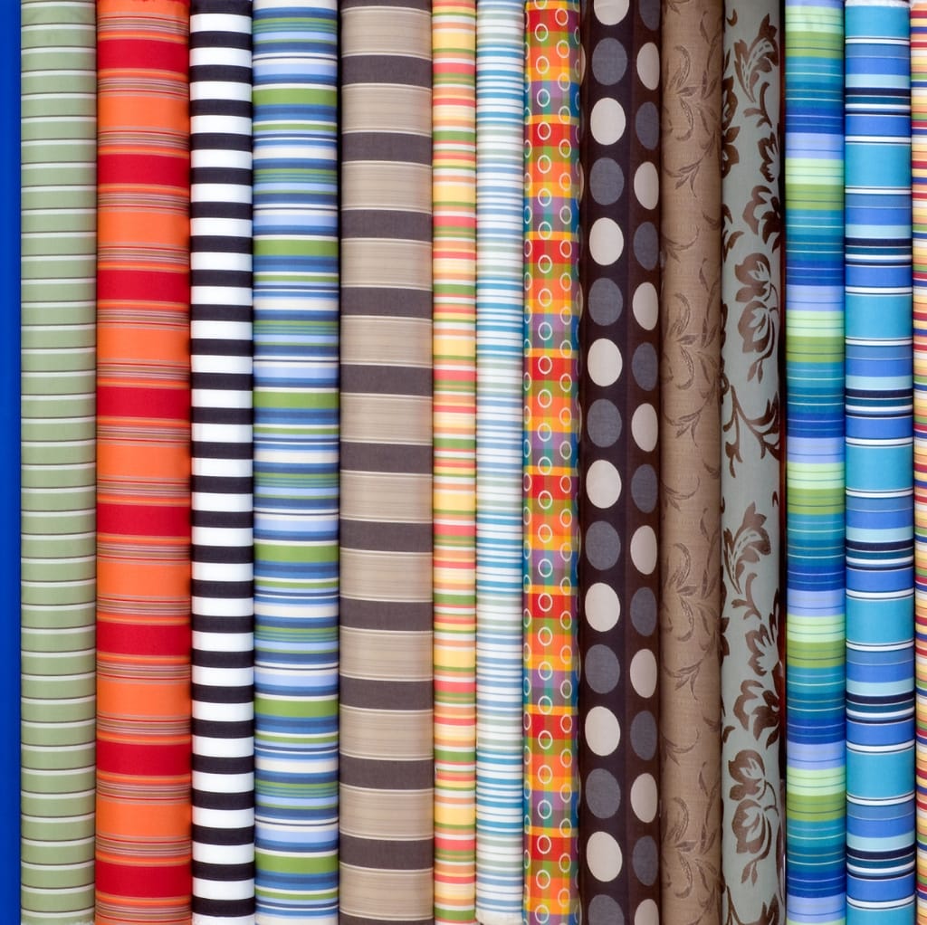 Colorful rolls of striped and patterned sateen cotton fabric stacked vertically.