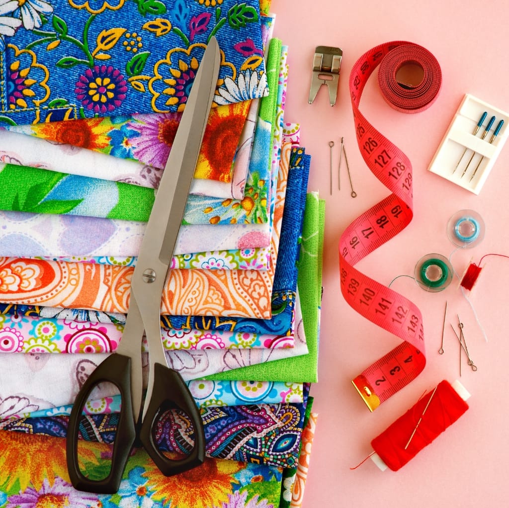 A vibrant workspace with colorful fabrics, sewing tools, and thread on a pink background, showcasing cotton lawn fabric.