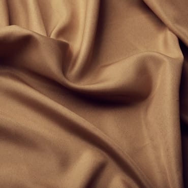 Close-up of smooth, beige polyester fabric with soft folds, ideal for stylish clothing.