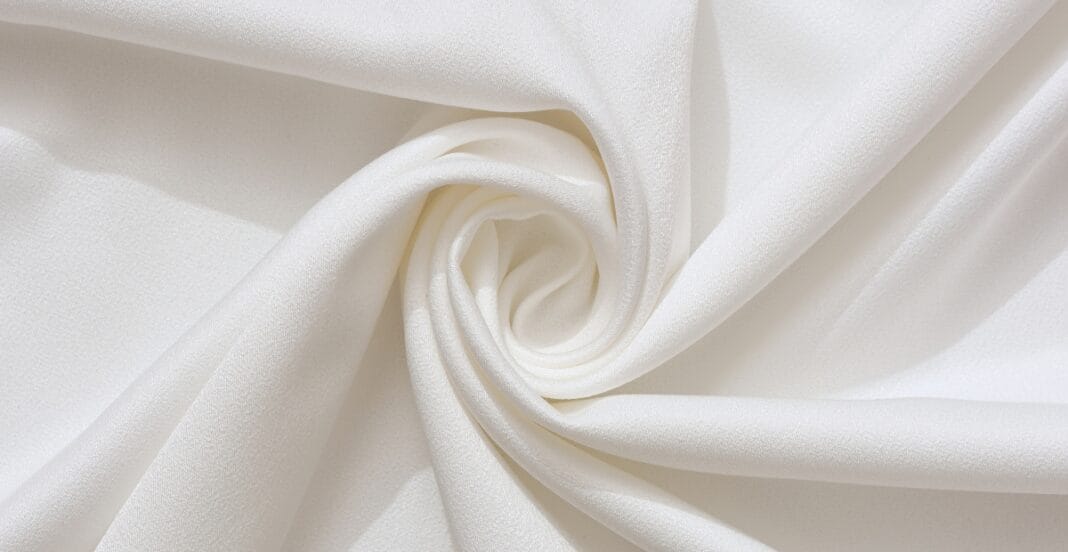 Close-up image of soft, white cotton fabric with a smooth, slightly textured surface, gently twisted in the center.