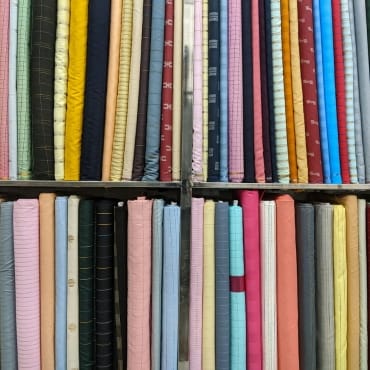 A large collection of neatly folded and arranged polyester fabrics on shelves, showcasing various colors and patterns.