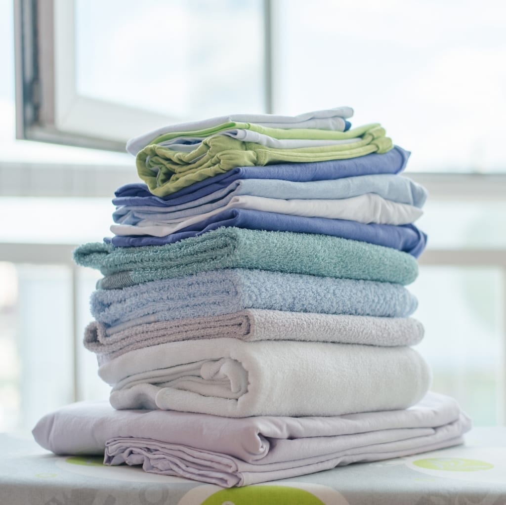 A neatly stacked pile of colorful cotton utility and cleaning cloths, including towels and rags, placed on a surface near a window. Bulk Cotton Fabric