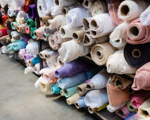 Stacks of colorful fabric rolls stored on shelves in a textile supplier warehouse.