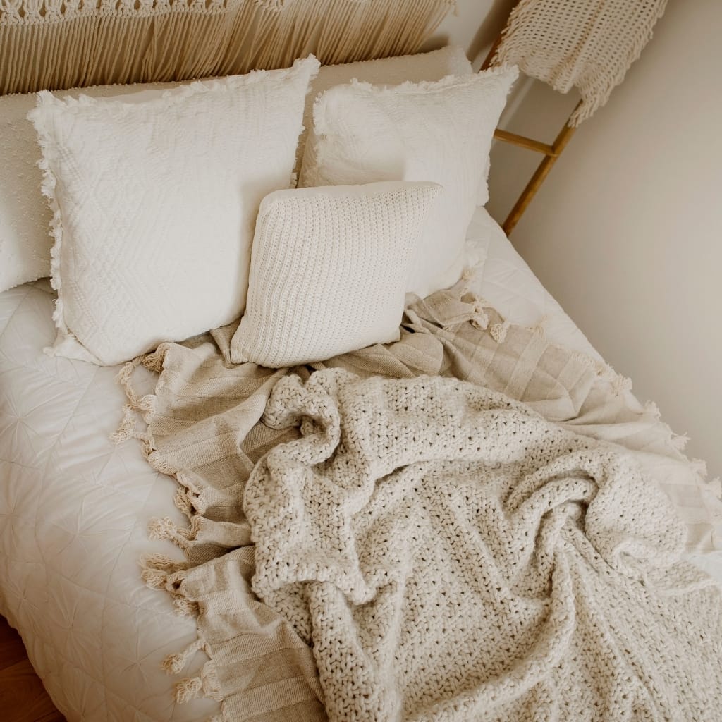 A cozy bedroom bed with white textured pillows, a chunky knit blanket, and neutral-toned bedding, creating a warm and inviting ambiance.