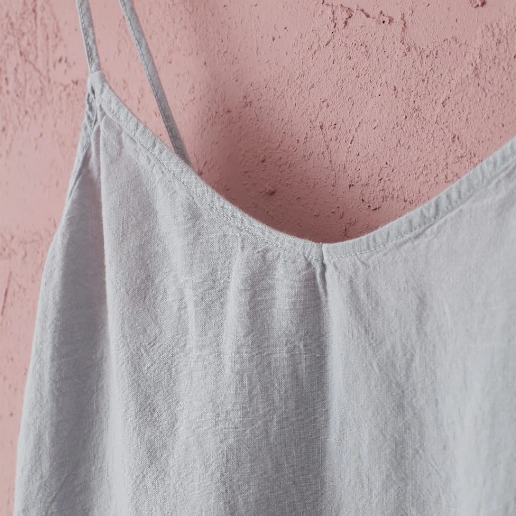 A close-up of a white fabric garment hanging on a pink textured wall.Caption: Close-up of a white fabric blouse or dress against a pink wall