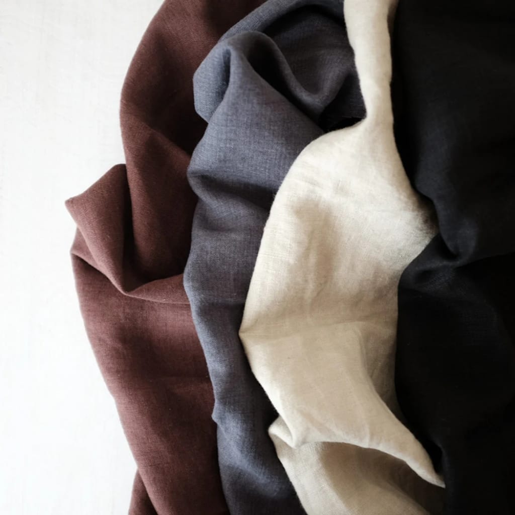 A close-up image of soft, folded fabric pieces in various colors including brown, gray, beige, and black.