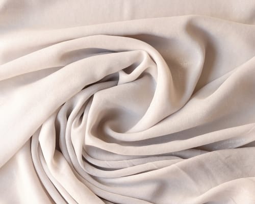 Close-up image of soft, cream-colored cotton fabric gently draped and swirled, showcasing its smooth texture.