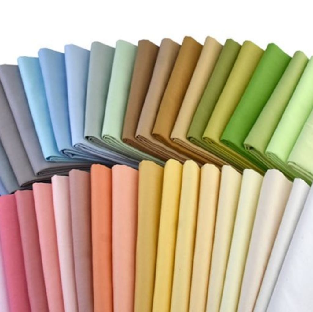 A neatly arranged display of rolled fabric in various pastel and neutral colors, forming a circular pattern.