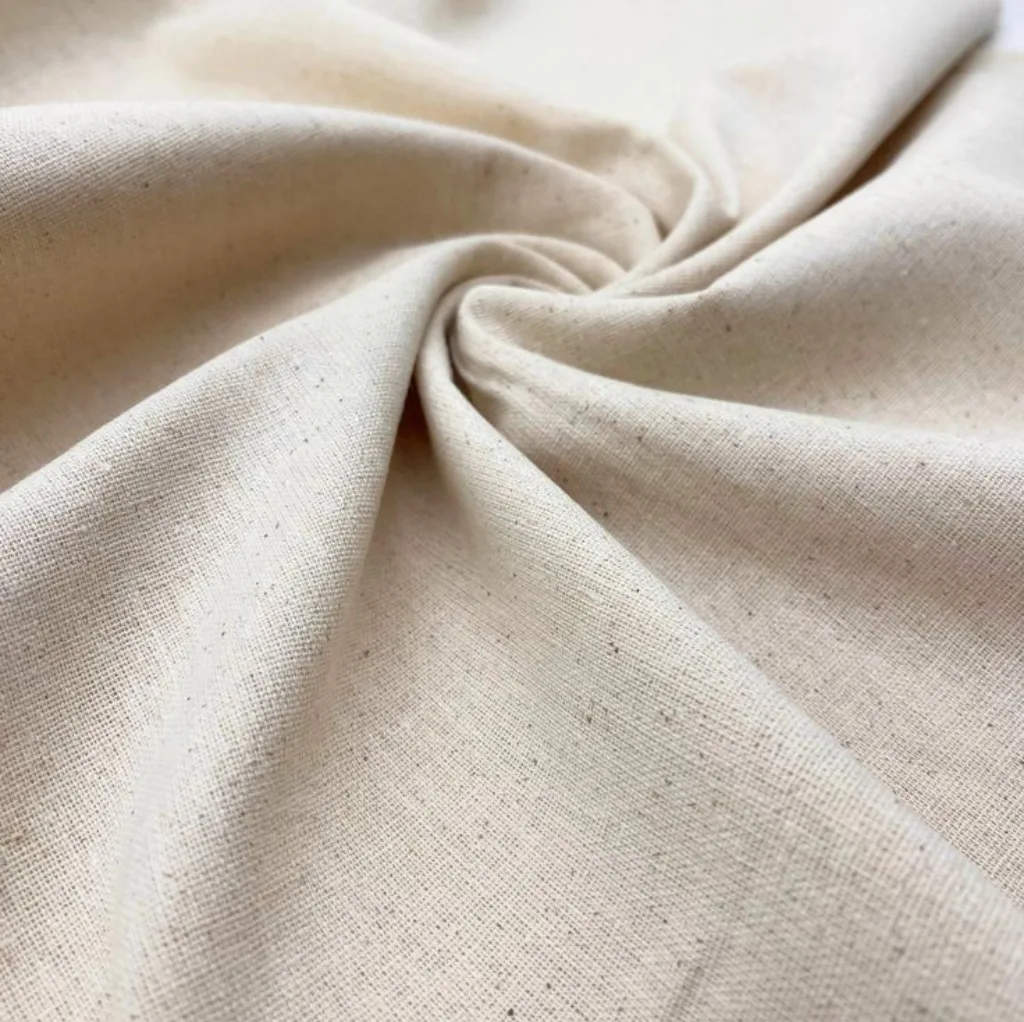 A close-up image of beige or natural-colored cotton fabric, gently twisted in the center, showcasing its soft texture and weave pattern.
