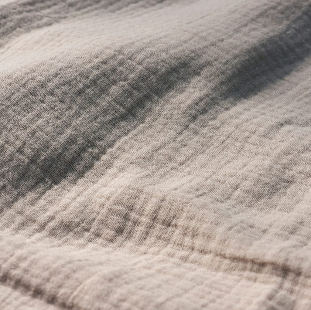 A close-up image of a soft, beige cotton muslin fabric with a textured, woven appearance.