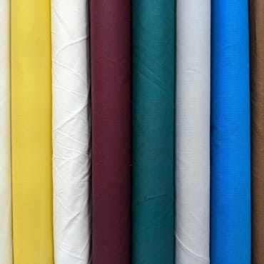 Assortment of colorful polyester fabric rolls in yellow, white, maroon, teal, silver, and blue, showcasing variety and affordable options suitable for sewing and craft projects.