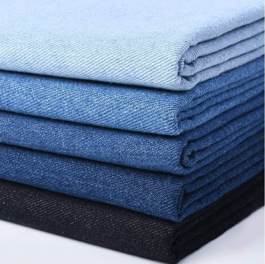 Stack of folded denim cotton fabrics in various shades of blue and black.