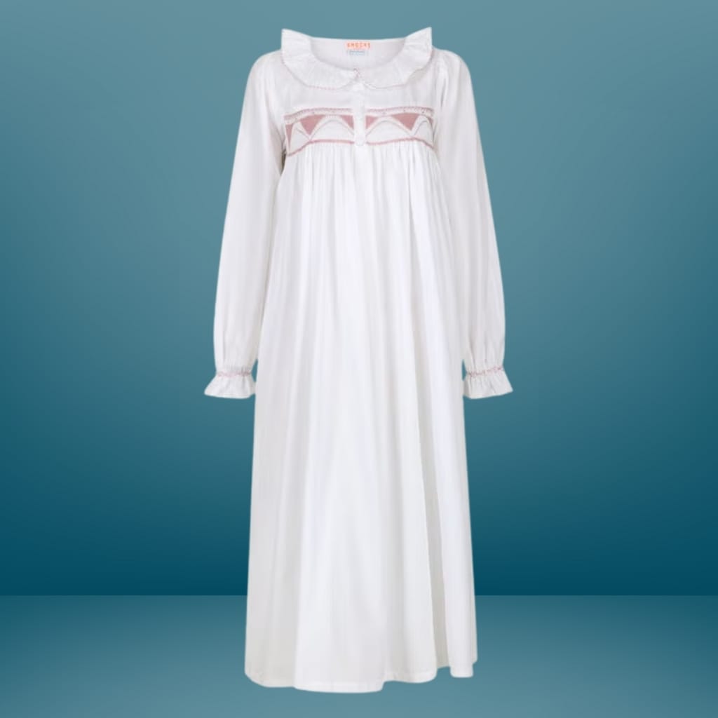 A long, white, embroidered nightgown or dress with long sleeves, ruffled cuffs, and a rounded collar, displayed against a blue background.
