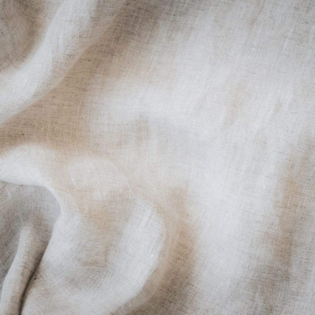 Close-up of light beige linen fabric with soft folds and subtle texture.