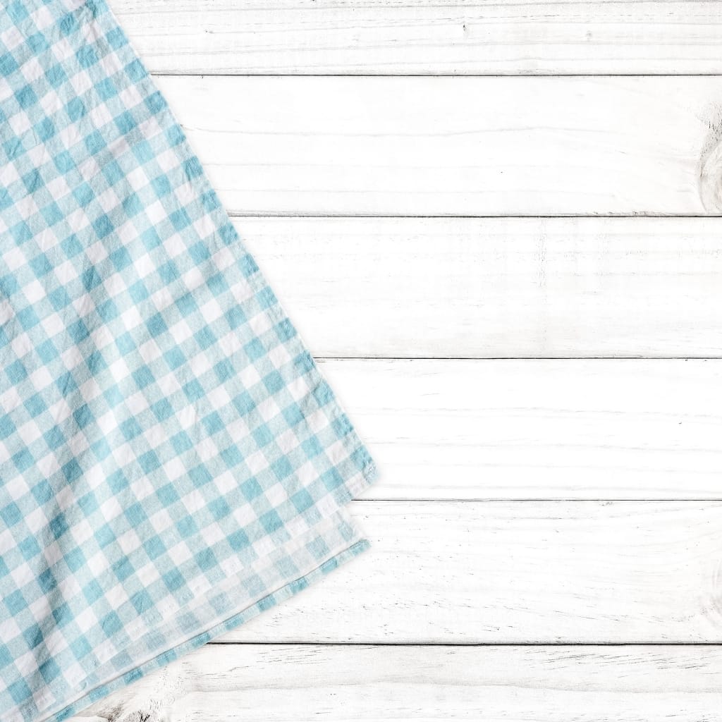 Light blue and white checkered cloth partially folded on a white wooden surface.