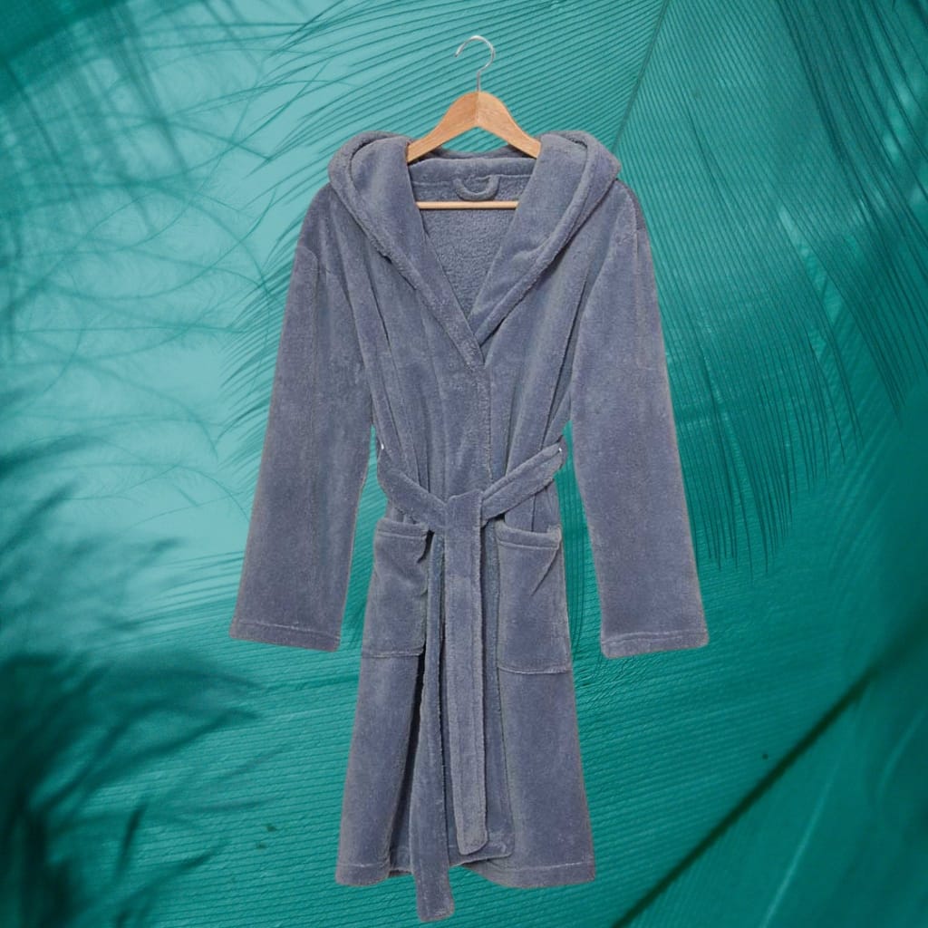 A gray bathrobe hanging on a wooden hanger against a background of green palm leaves.