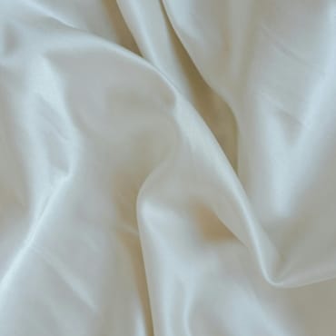 Close-up of soft, cream-colored polyester silk blend fabric with gentle folds and a smooth, shiny surface.