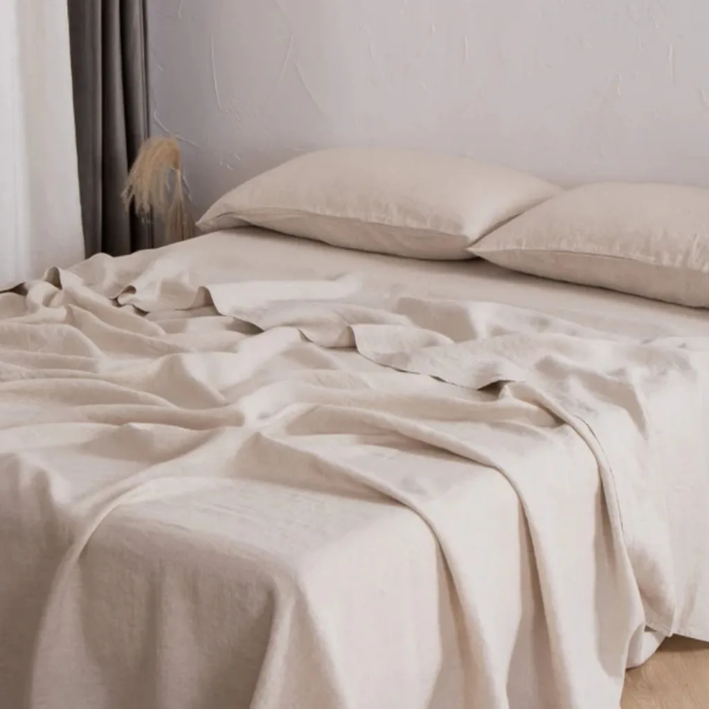 A neatly made bed with cream-colored bedsheets and two matching pillows on a white wall background. There are some folds and slight wrinkles on the bedsheets, giving a cozy and inviting appearance.