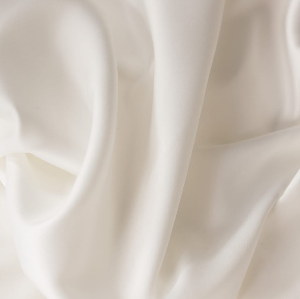 Close-up of smooth, ivory-colored fabric with a soft sheen, showcasing its fine texture and gentle drape.